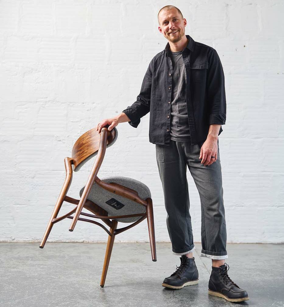 Justin Nelson in his warehouse holding one of his handmade chairs