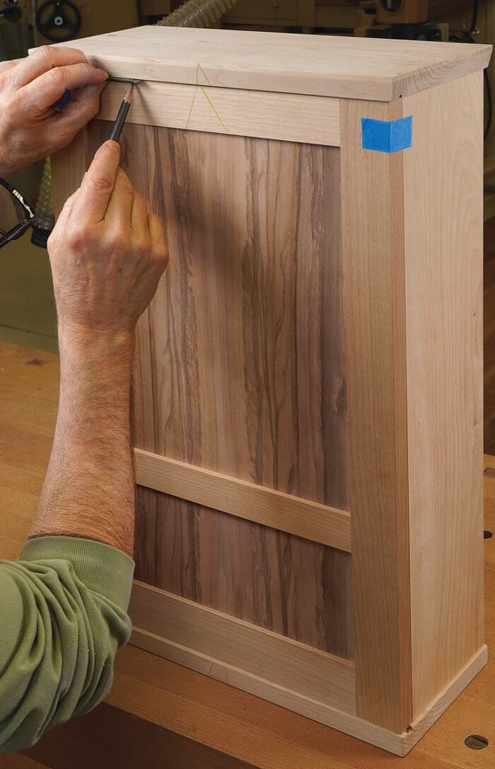 Fit the door. Using a crosscut sled, trim the lower edge of the door so it just fits between the case top and bottom and the hinge edge aligns with the side of the case. Then with the door resting on the bottom of the case, use a 11⁄1616-in. spacer to mark the trim line on the top edge of the door, as shown. This will give you a 11⁄3232-in. gap at the top and bottom edge. Leave the latch side of the door a bit overlong at this point.